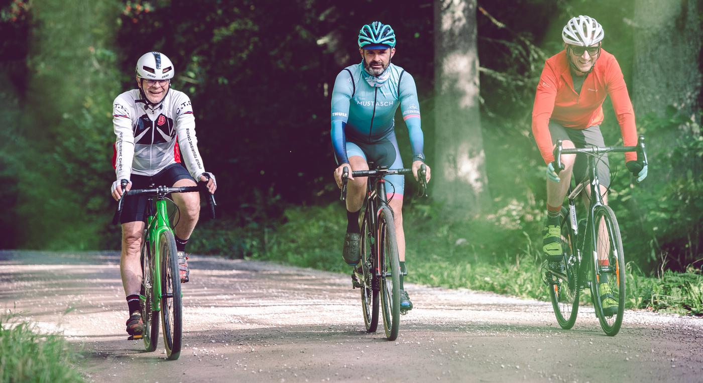 Tre personer cyklar på en grusväg i skogslandskap.