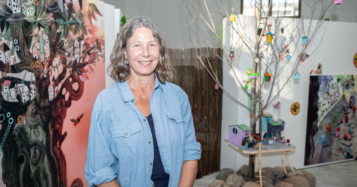 En kvinna står framför stora upptryckta illustrationer i en utställning.