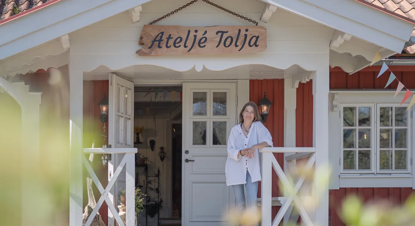 En kvinna som står framför en röd och vit byggnad med en skylt där det står Ateljé Tolja.