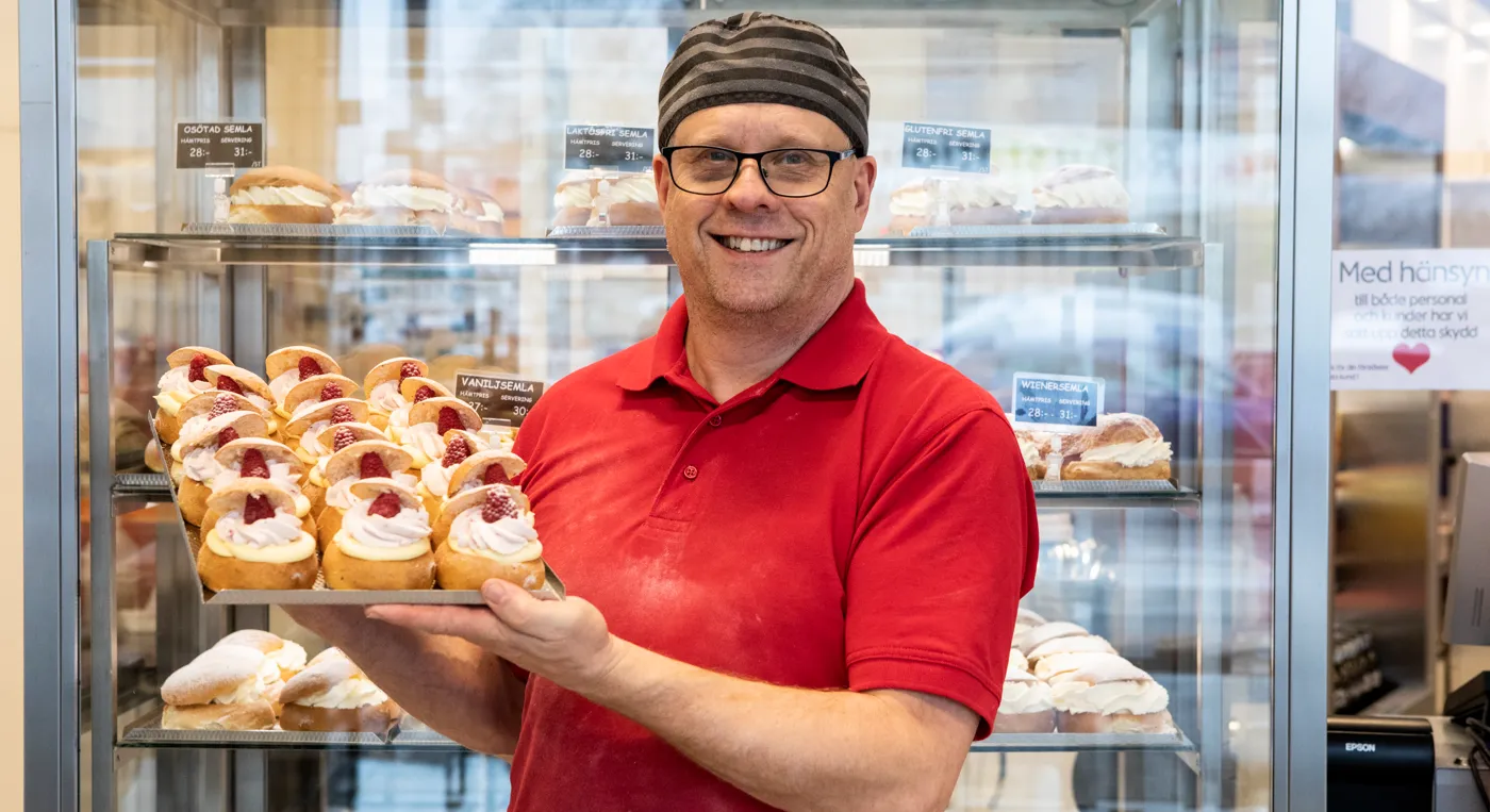 En man som håller i en bricka med bakverk i ett bageri.