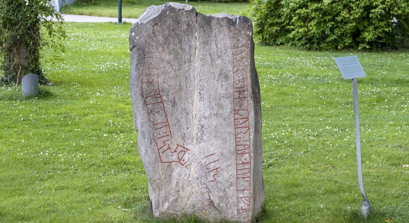 En stor runsten som ligger mitt i ett grönskande fält.