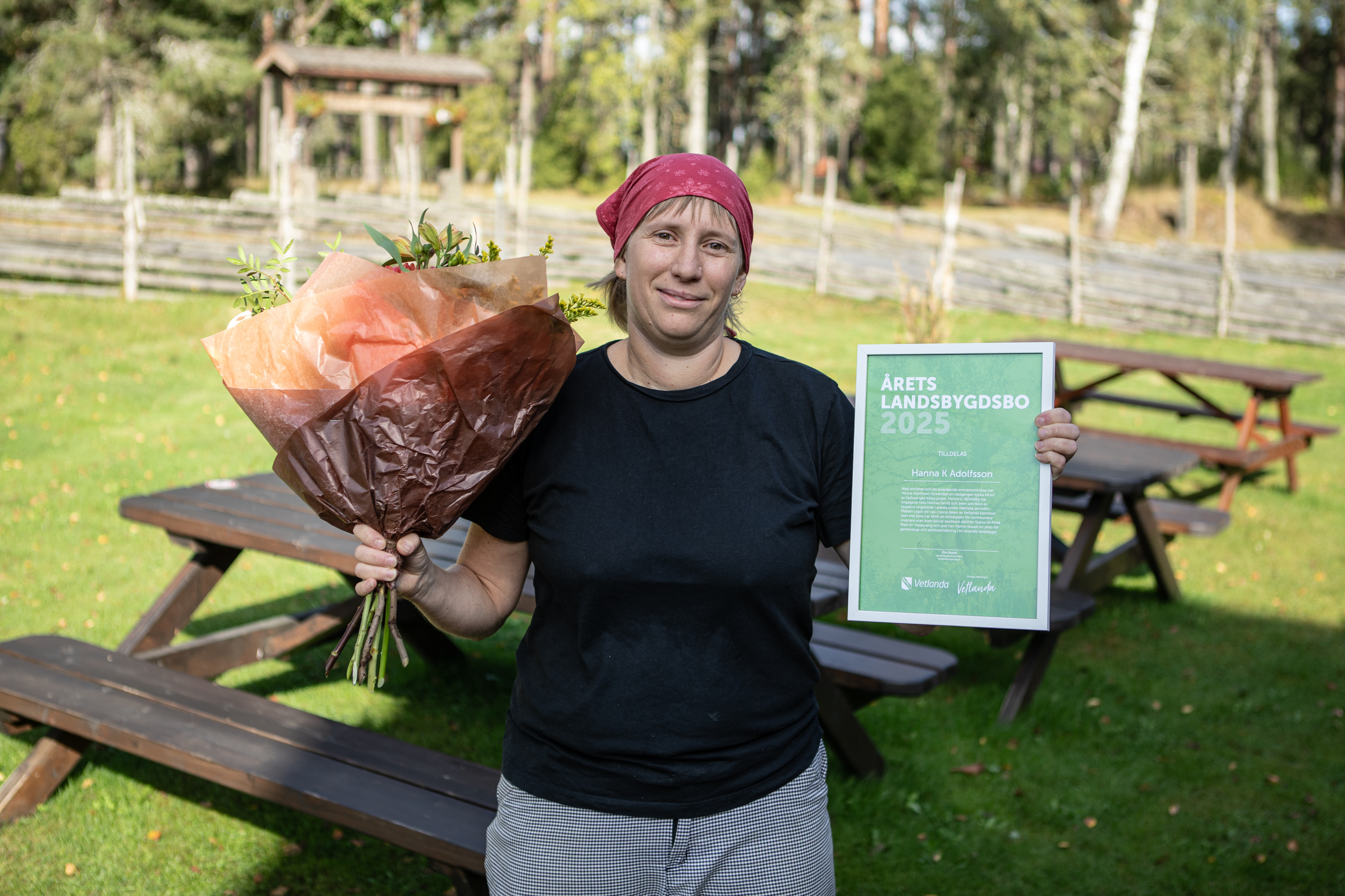 En kvinna håller i en blombukett framför ett picknickbord.