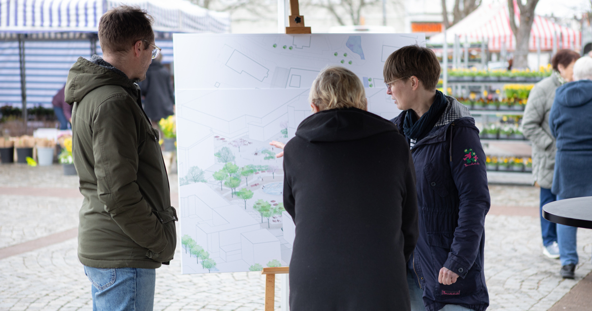Tre personer står framför en stor skiss över Stortorget i Vetlanda. En ser ut att peka på bilden och visa något för en av de andra.
