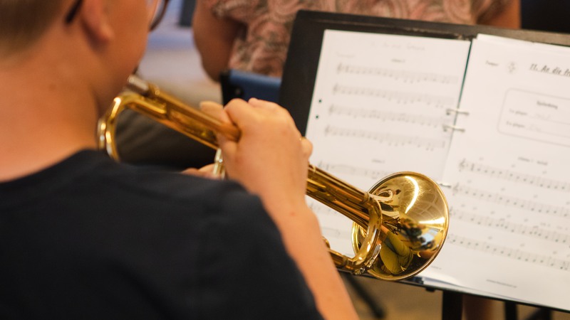 Närbild på elev som blåser i en trumpet och tittar på noter samtidigt.