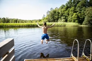 En pojke hoppar ner i vattnet från en brygga