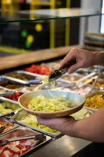 En person plockar sallad från en salladsbar