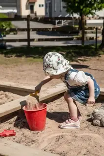Ett barn gräver med en spade och häller sand i en hink.